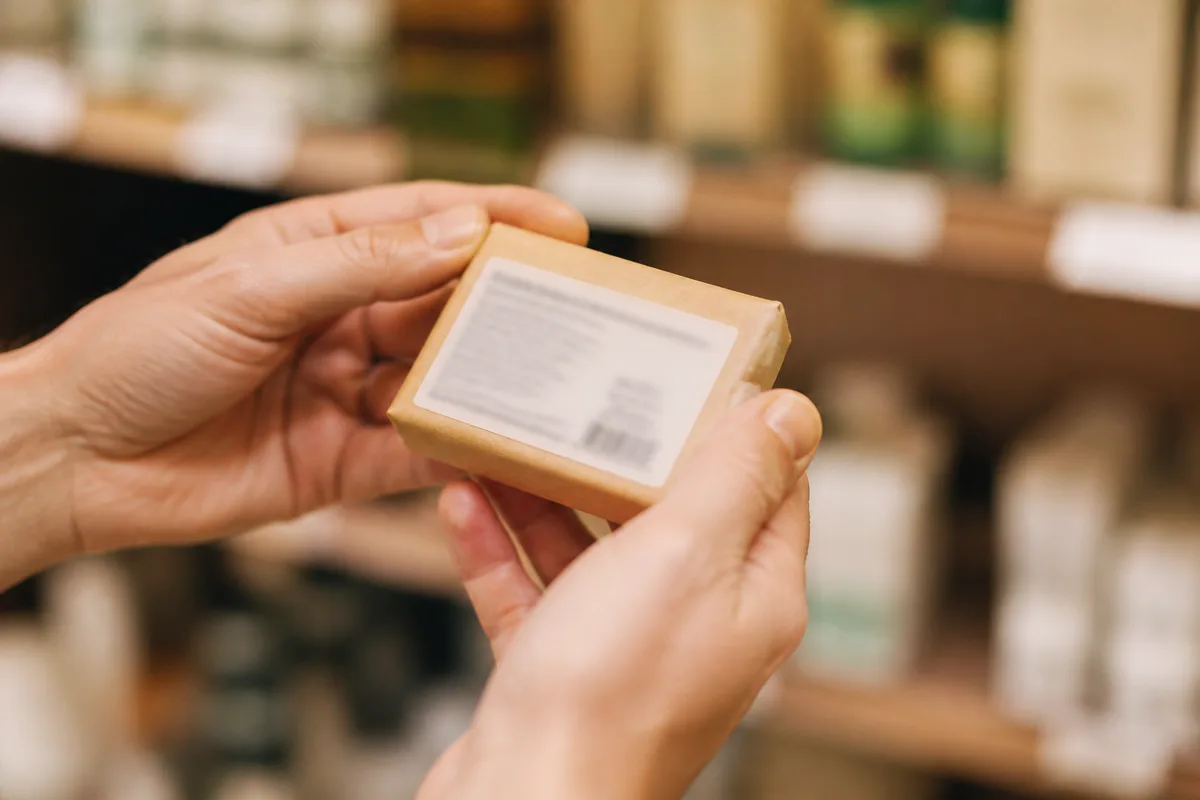 Main tenant un savon retourné pour lire la liste des ingrédients imprimée sur son emballage papier